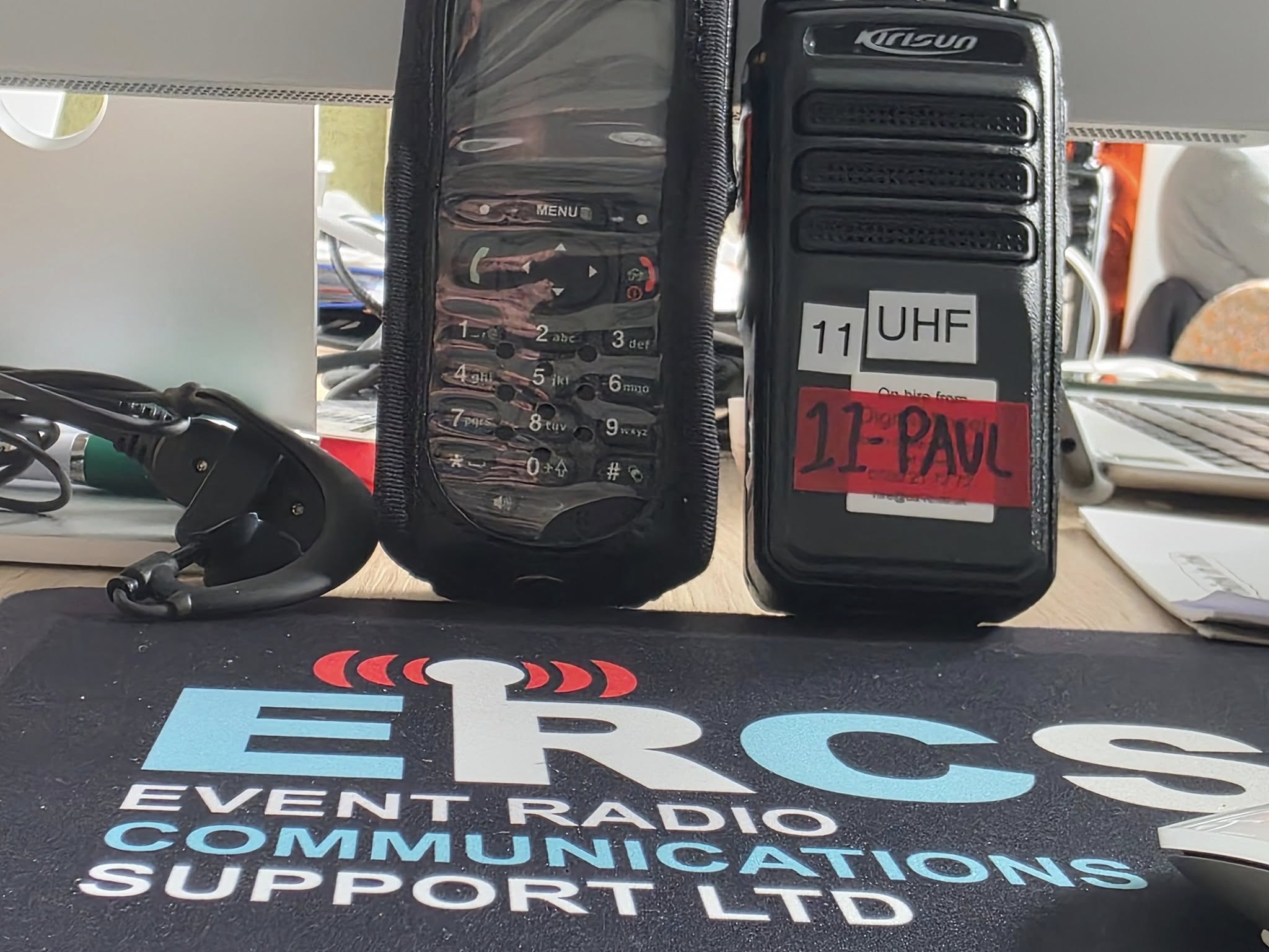 ERCS control desk showing a live precipitation radar over Scotland on an iMac display, with a Motorola mobile base radio and Kirisun UHF handset in front, branded ERCS mousepad on the desk.